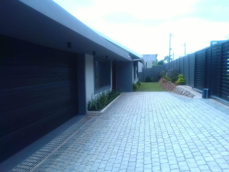 Modern exterior view featuring a paved driveway, automated garage door, and landscaped retaining wall along the boundary fence.