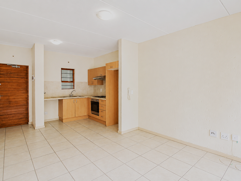An open-plan living and kitchen area featuring tiled flooring, built-in wooden cabinetry, integrated oven and hob, and a solid wood entrance door.