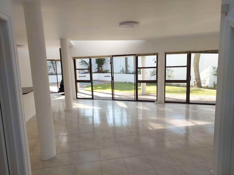 Spacious open-plan living area featuring tiled floors, structural columns, and large sliding glass doors providing direct access to the garden and pool area.