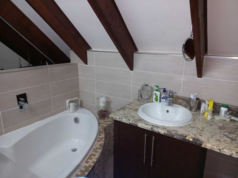 A well-maintained bathroom featuring a built-in bathtub, stone-topped vanity, and distinctive exposed timber rafters under a pitched ceiling.