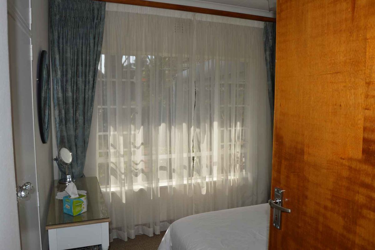 A bedroom featuring a large window with sheer curtains, built-in cupboard space, and neutral carpeting.