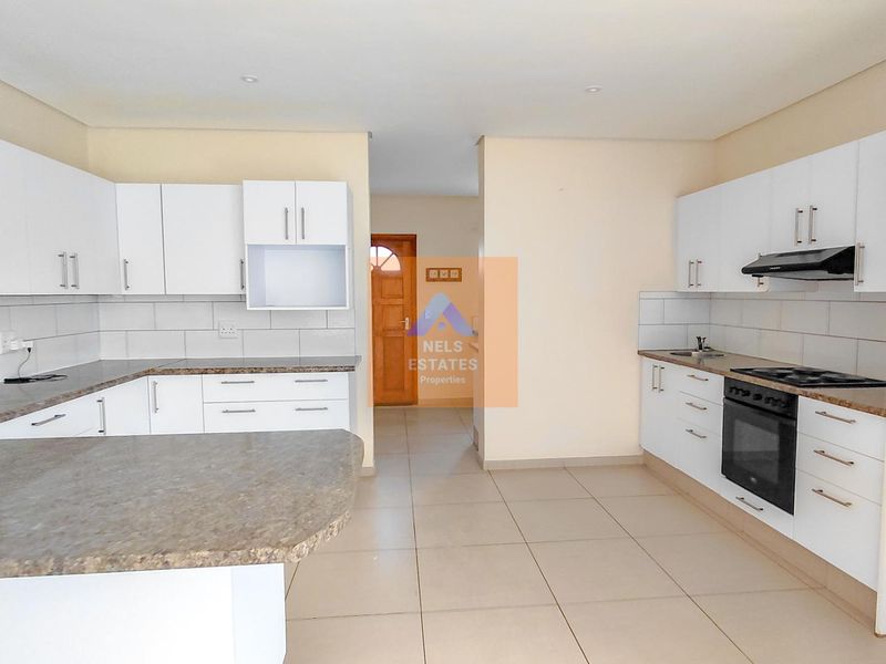 A clean, modern kitchen featuring white cabinetry, granite countertops, built-in oven, hob, and extractor fan, with neutral tiled flooring throughout.