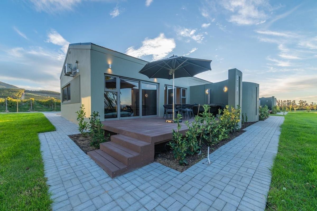 A modern exterior view of a commercial unit featuring a private timber deck, paved walkways, and landscaped surroundings with scenic vineyard views.