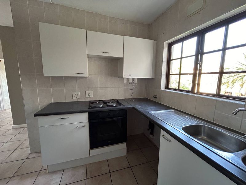 A functional kitchen featuring white built-in cabinetry, dark laminate countertops, an integrated electric hob and oven, and a stainless steel sink with tiled finishes.