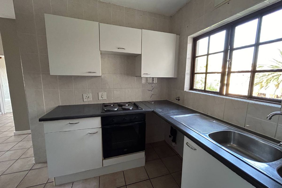 A functional kitchen featuring white built-in cabinetry, dark laminate countertops, an integrated electric hob and oven, and a stainless steel sink with tiled finishes.