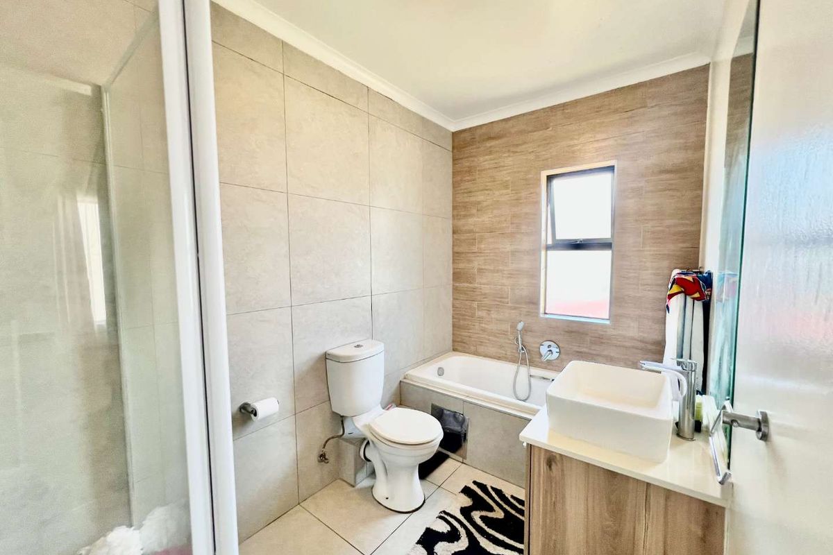 Modern bathroom featuring a built-in bathtub, separate glass-enclosed shower, vanity basin, and contemporary neutral wall tiling.