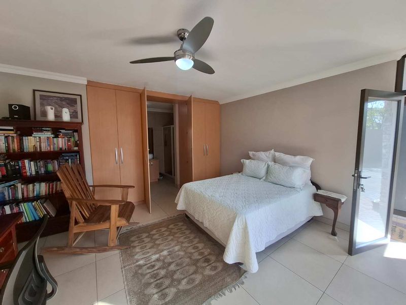 A well-maintained bedroom featuring built-in cupboards, a ceiling fan, tiled flooring, and direct access to an en-suite bathroom.