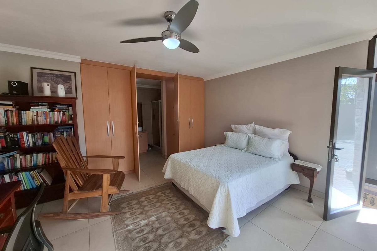 A well-maintained bedroom featuring built-in cupboards, a ceiling fan, tiled flooring, and direct access to an en-suite bathroom.
