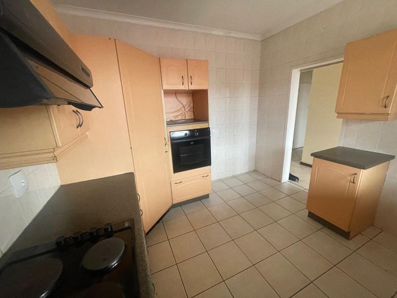 A functional kitchen featuring built-in cabinetry, an integrated oven, electric hob, and extractor fan, finished with tiled flooring and splashbacks.