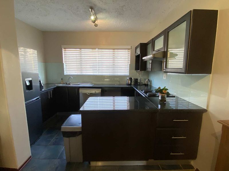 A functional kitchen featuring dark wood cabinetry, granite countertops, a glass splashback, and integrated appliances, offering a practical layout for daily use.
