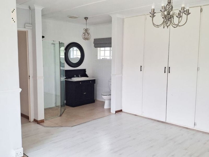 Spacious bedroom featuring light laminate flooring, extensive built-in cupboards, and an open-plan en-suite bathroom with a shower, vanity, and toilet.