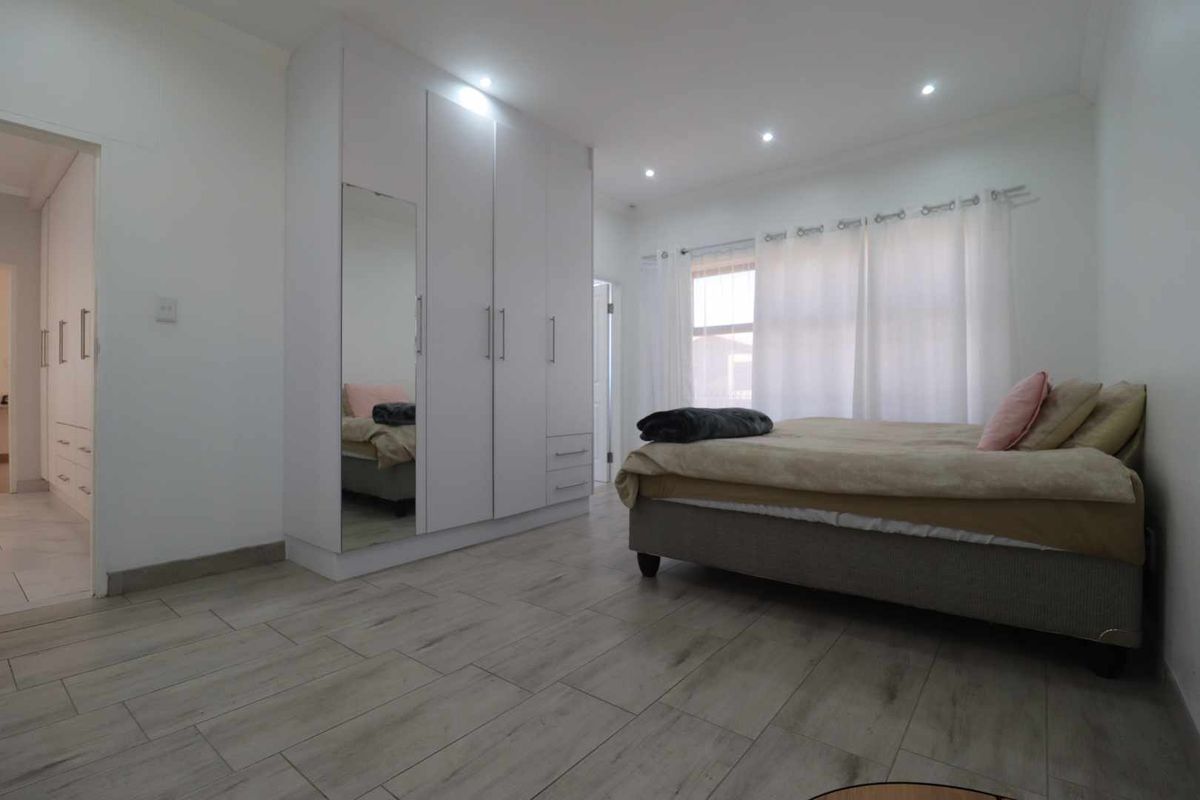 A bright bedroom featuring modern wood-look tile flooring, recessed ceiling lighting, and a large built-in wardrobe with a mirrored panel.