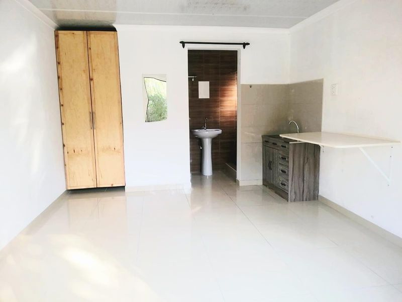 An open-plan studio space featuring a kitchenette with cabinetry, a built-in wardrobe, and an adjoining bathroom with a pedestal sink.