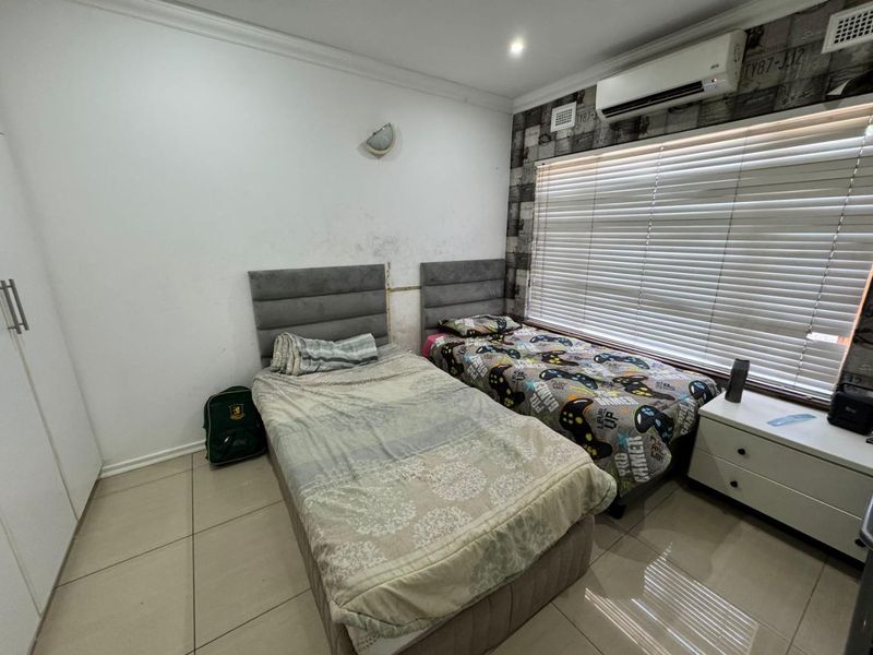 A bedroom featuring tiled flooring, built-in cupboards, and an air conditioning unit, currently showing signs of wall staining and dated wallpaper finishes.