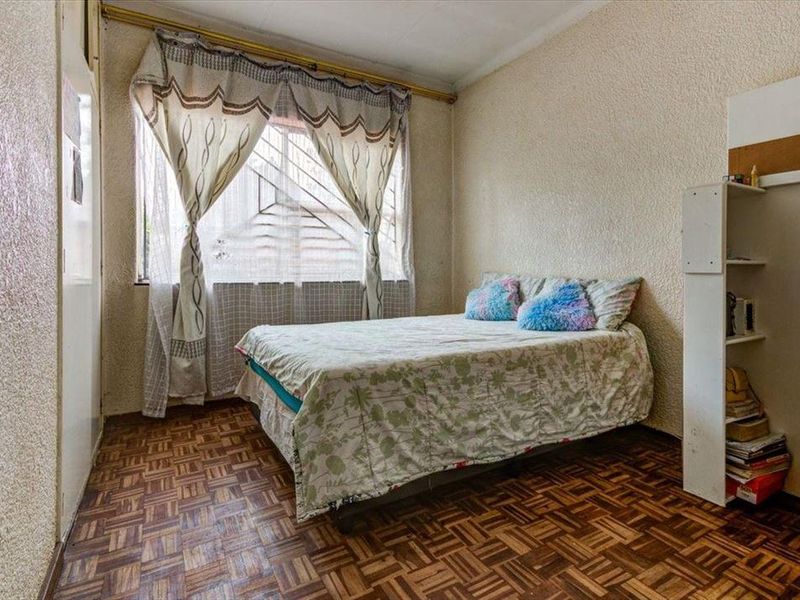 A bedroom featuring parquet flooring, security bars on the window, and built-in shelving, offering a functional space with potential for cosmetic updates.