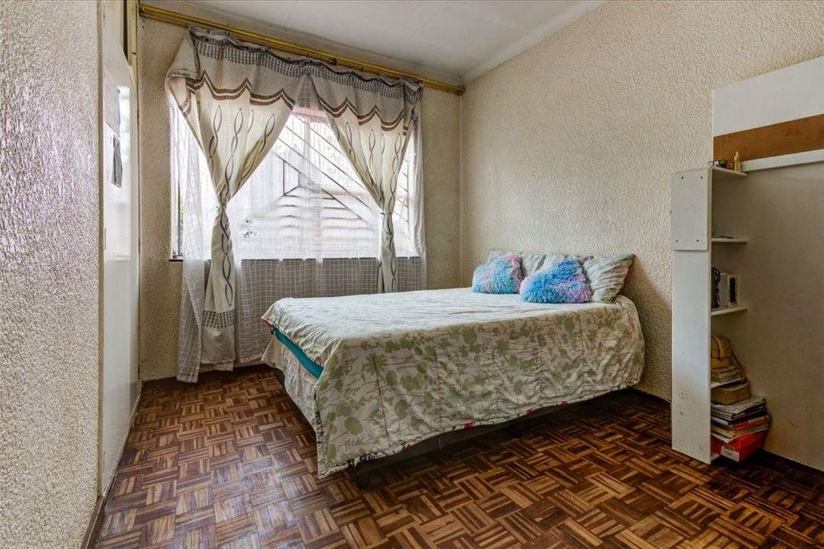 A bedroom featuring parquet flooring, security bars on the window, and built-in shelving, offering a functional space with potential for cosmetic updates.