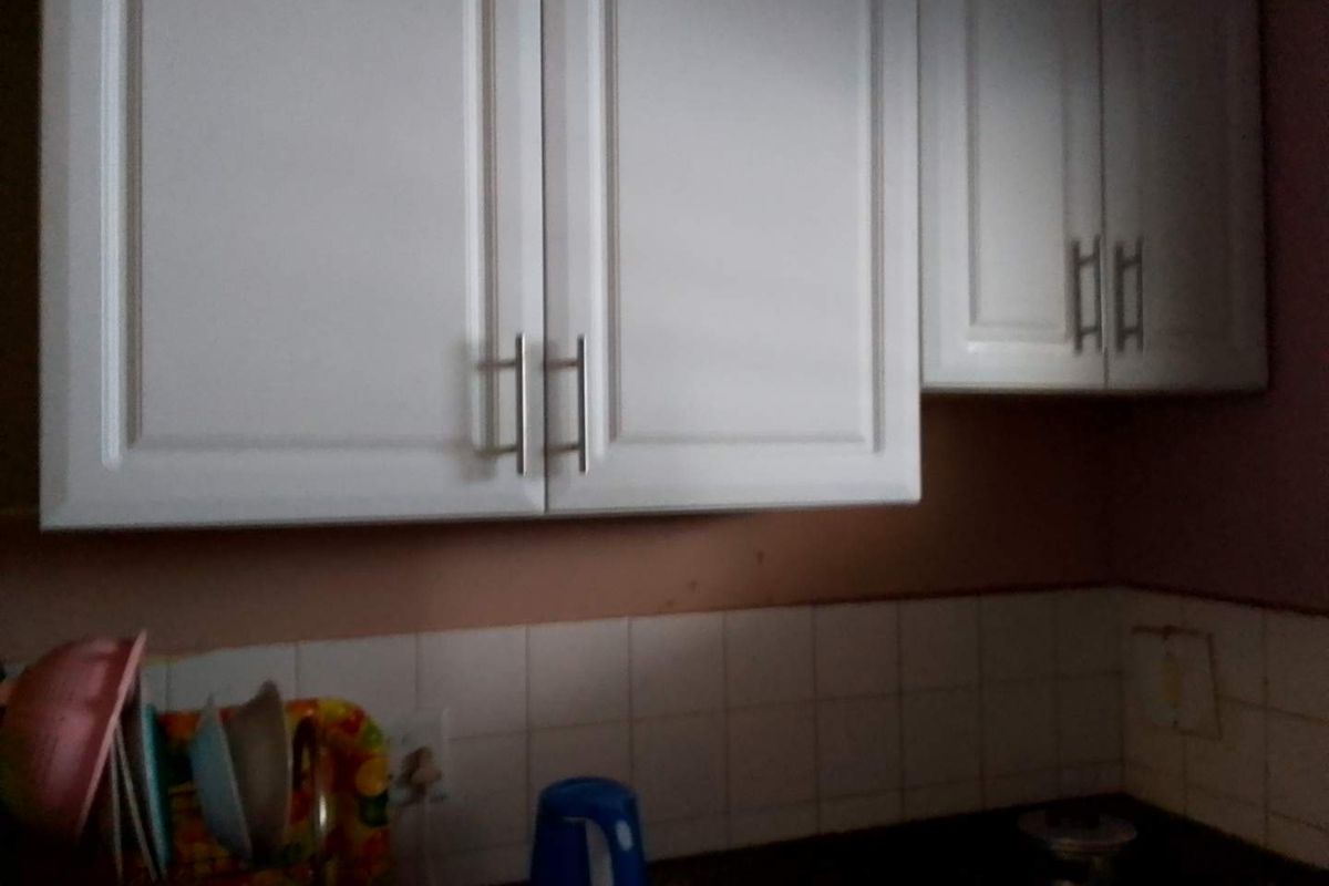A close-up view of kitchen cabinetry with white doors, a tiled backsplash, and a dark countertop in need of cosmetic updates.
