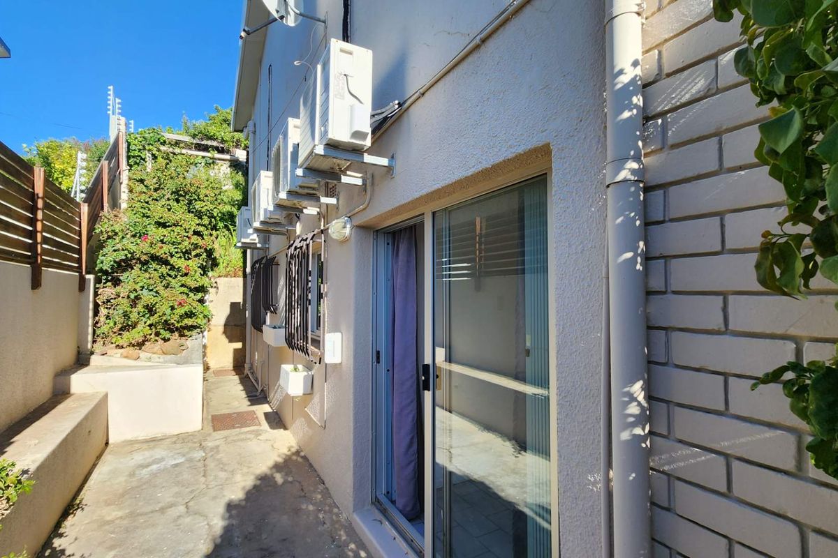 A narrow rear exterior walkway featuring concrete paving, a sliding glass door, and multiple wall-mounted air conditioning units.