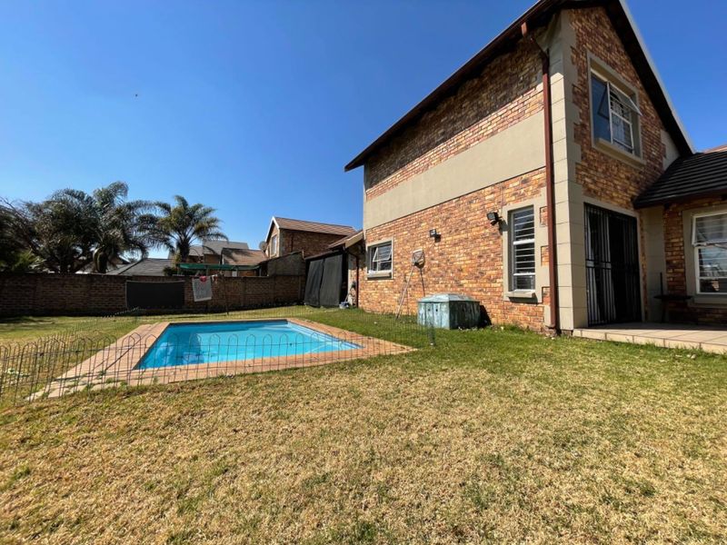 Rear view of the cluster property featuring a private swimming pool, brick exterior facade, and a fenced garden area.