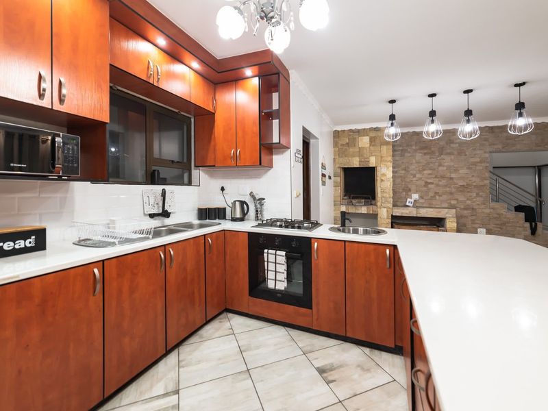 Open-plan kitchen featuring warm wood cabinetry, stone-clad feature wall with indoor braai, and modern tiled flooring, seamlessly connecting to the living area.