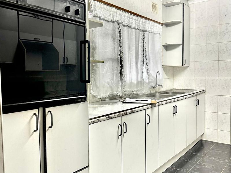 A functional kitchen featuring built-in cabinetry, a wall-mounted oven, laminate countertops, and tiled finishes throughout, offering potential for a modern renovation.