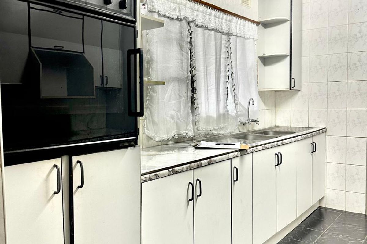 A functional kitchen featuring built-in cabinetry, a wall-mounted oven, laminate countertops, and tiled finishes throughout, offering potential for a modern renovation.