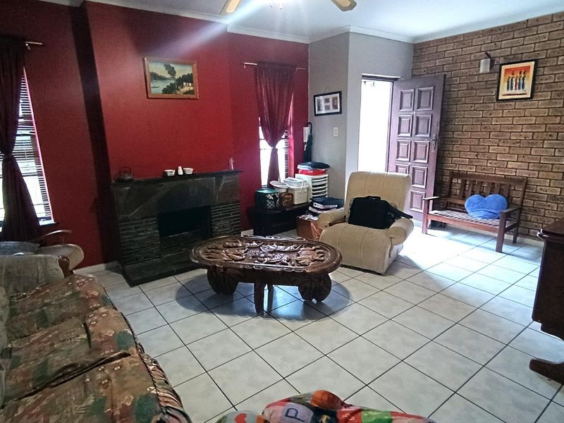 A living room featuring a stone fireplace, an exposed brick feature wall, and ceramic floor tiles, offering a traditional layout with natural light.