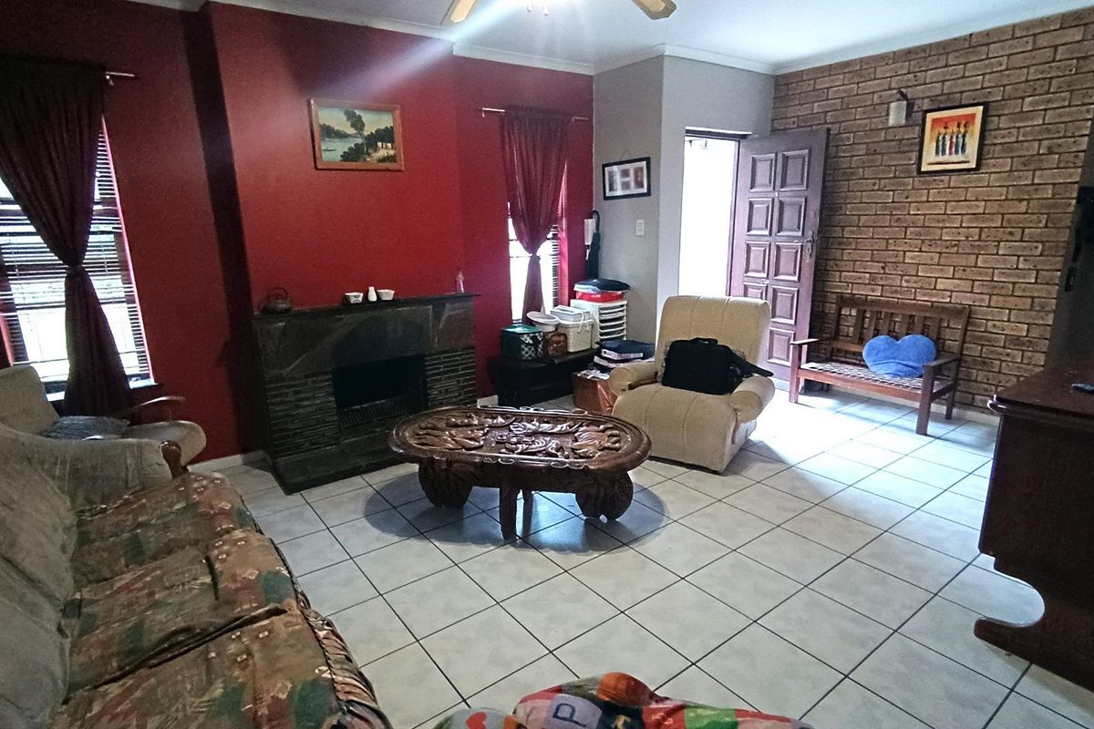 A living room featuring a stone fireplace, an exposed brick feature wall, and ceramic floor tiles, offering a traditional layout with natural light.