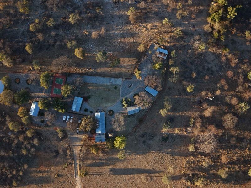 Aerial view of the lodge property featuring multiple structures, a tennis court, and established pathways set within a natural bushveld landscape.