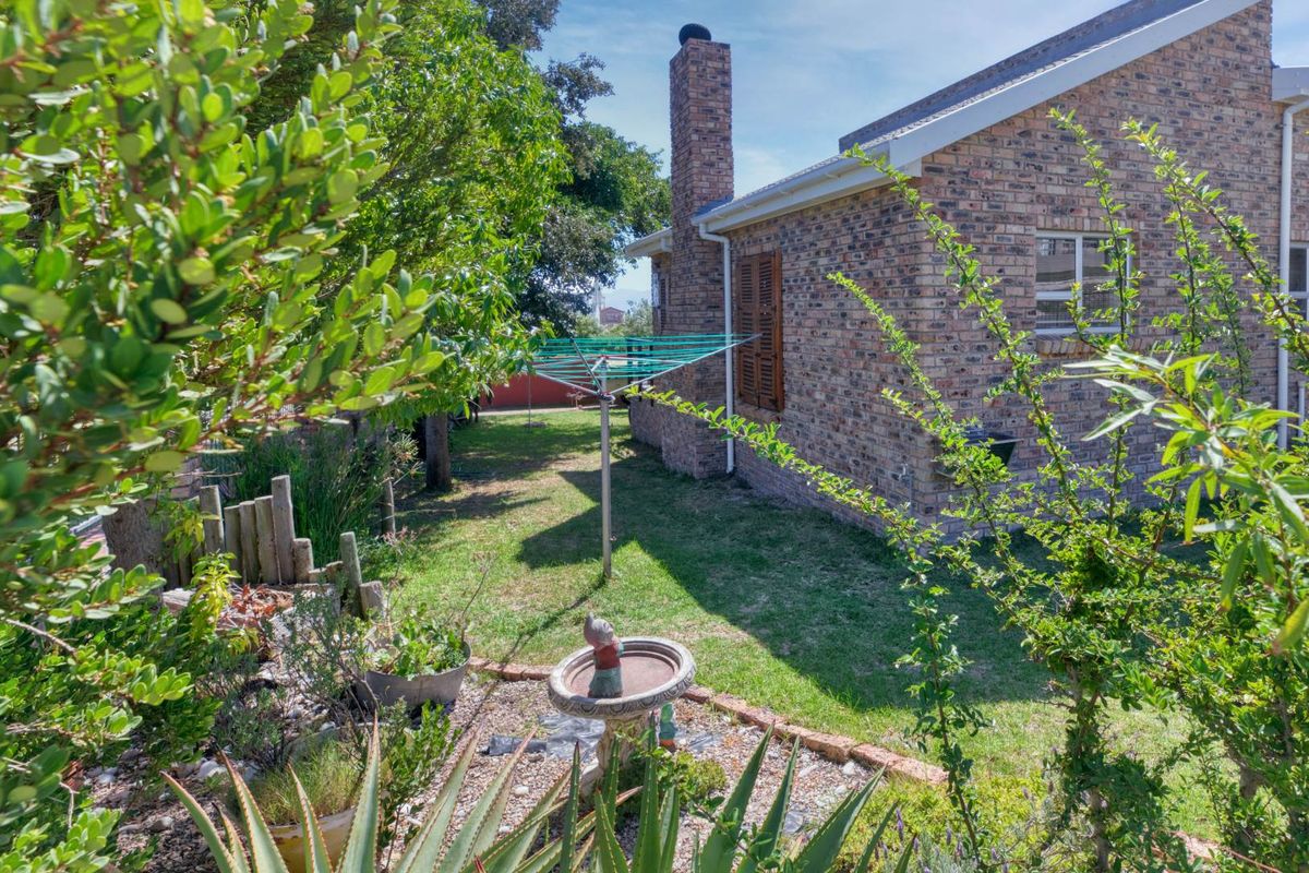 A view of the rear garden featuring a brick exterior wall, a tall brick chimney, and established landscaping.
