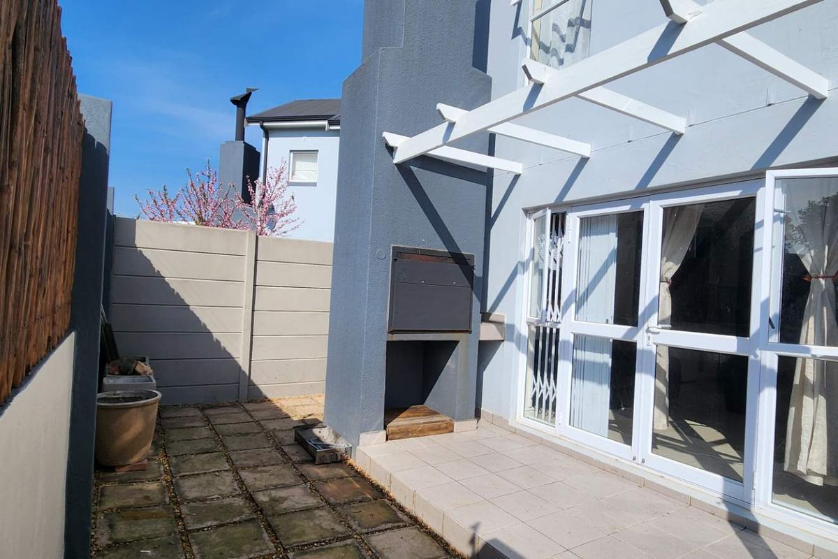 Rear patio area featuring a built-in braai, white pergola structure, and paved flooring, providing a functional outdoor entertainment space.