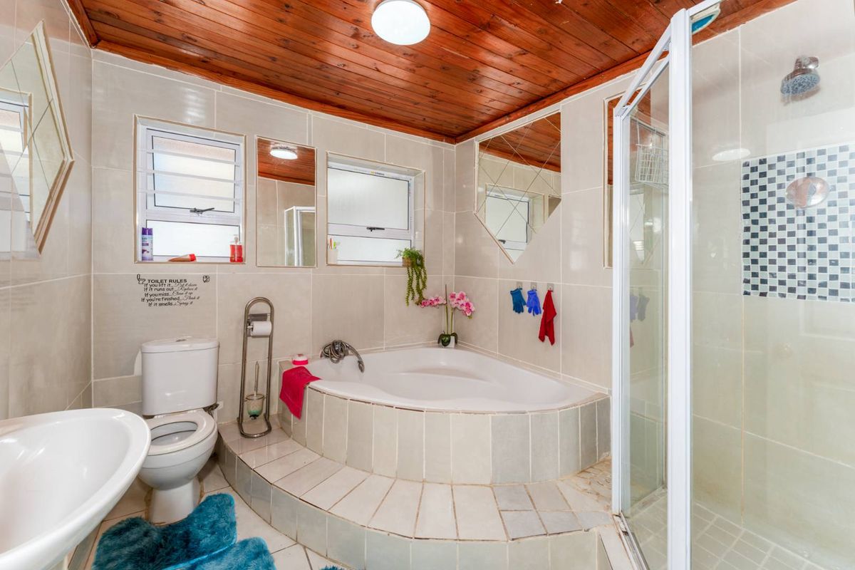 A bathroom featuring a raised corner bathtub, a separate shower enclosure, a toilet, and a vanity basin, finished with tiled walls and a timber ceiling.