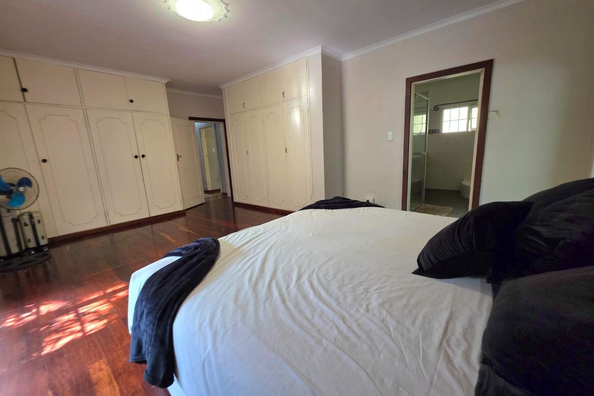 Spacious bedroom featuring extensive built-in cabinetry, polished hardwood flooring, and an en-suite bathroom access.
