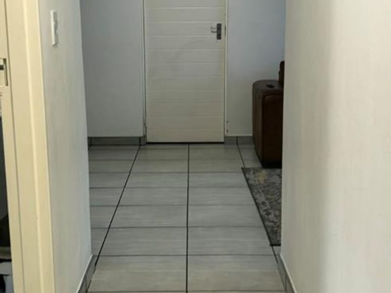 A clean, neutral hallway featuring light grey floor tiles, recessed ceiling lighting, and a simple interior door leading to an adjacent room.