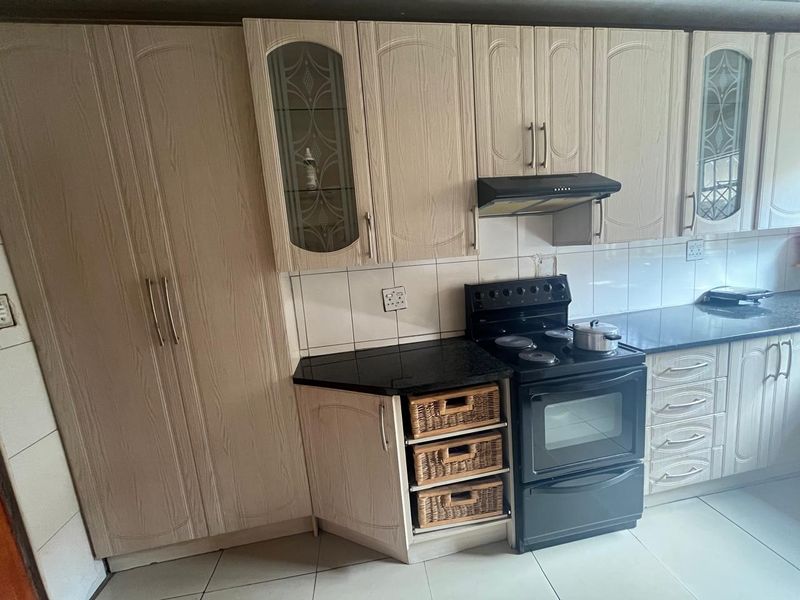 A functional kitchen featuring light wood-finish cabinetry, black granite countertops, a built-in stove with extractor fan, and tiled flooring.
