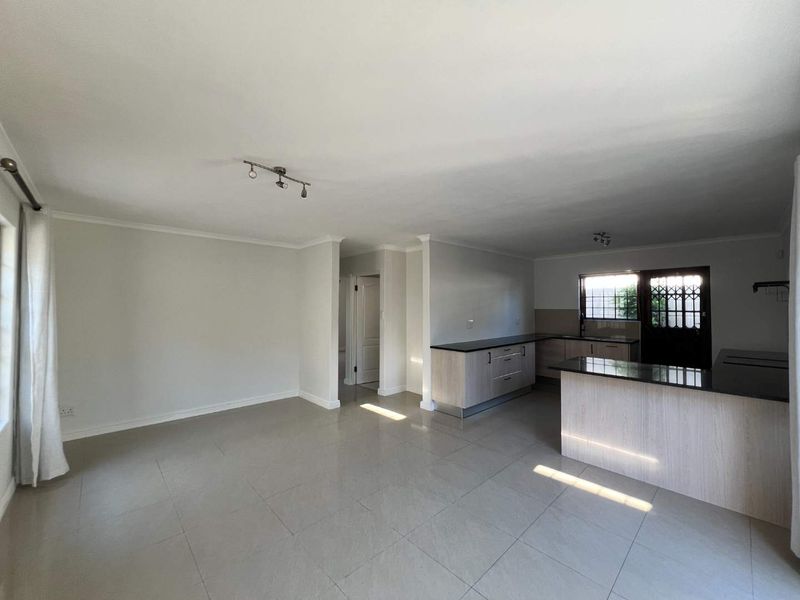Spacious open-plan living and kitchen area featuring neutral tiled flooring, modern cabinetry with granite countertops, and direct access to the exterior.