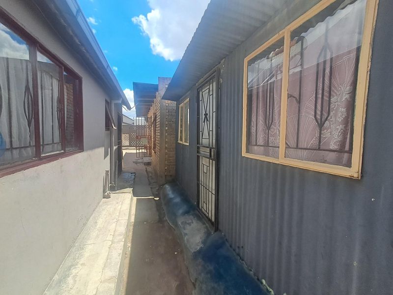 A narrow exterior side passage between two structures featuring corrugated metal siding, security gates, and concrete paving.