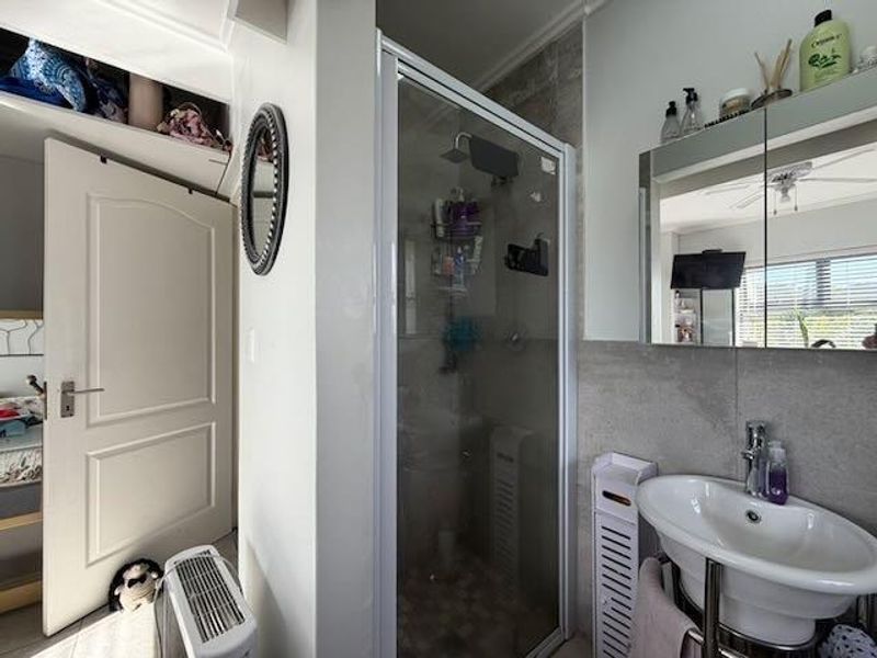 A functional bathroom featuring a glass-enclosed shower, a pedestal basin with a mixer tap, and a mirrored medicine cabinet with tiled wall finishes.