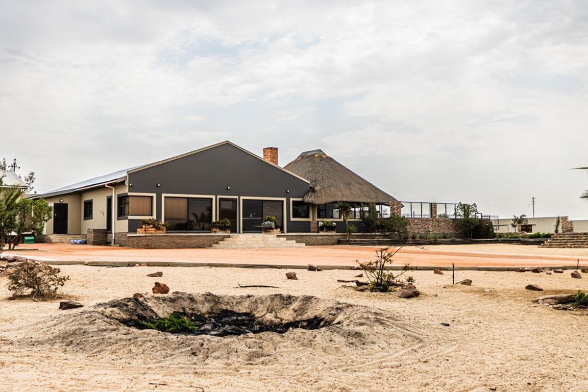 Rear view of the small holding featuring a combination of modern metal roofing and traditional thatch, with sliding doors leading onto a paved patio area.