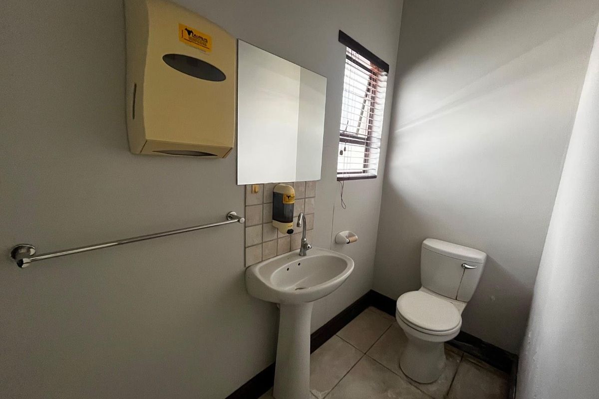 A functional office restroom featuring a pedestal sink, wall-mounted mirror, toilet, and tiled flooring.