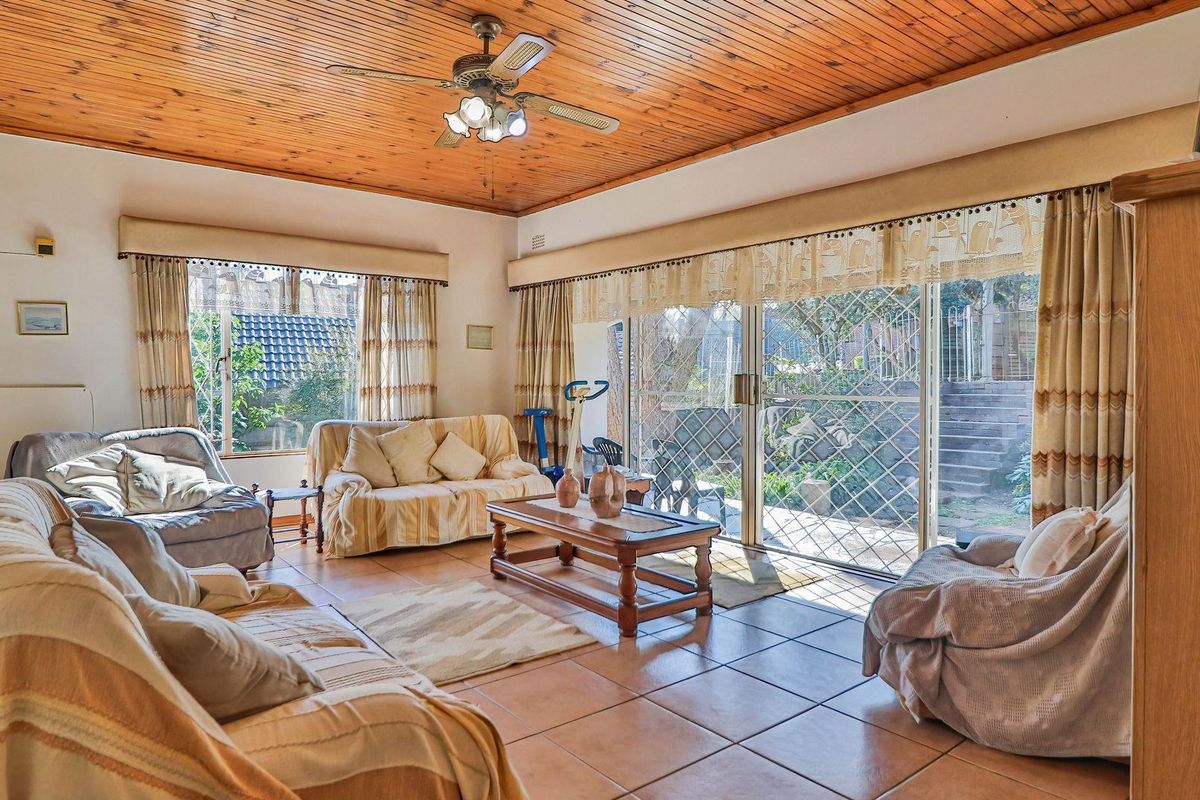 Spacious living room featuring a warm timber-clad ceiling, tiled flooring, and large sliding glass doors that provide direct access to the rear garden.