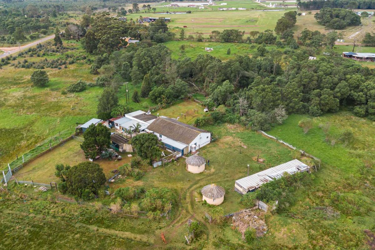 Aerial view of a small holding property featuring a main dwelling, two thatched rondavels, outbuildings, and expansive surrounding grounds.