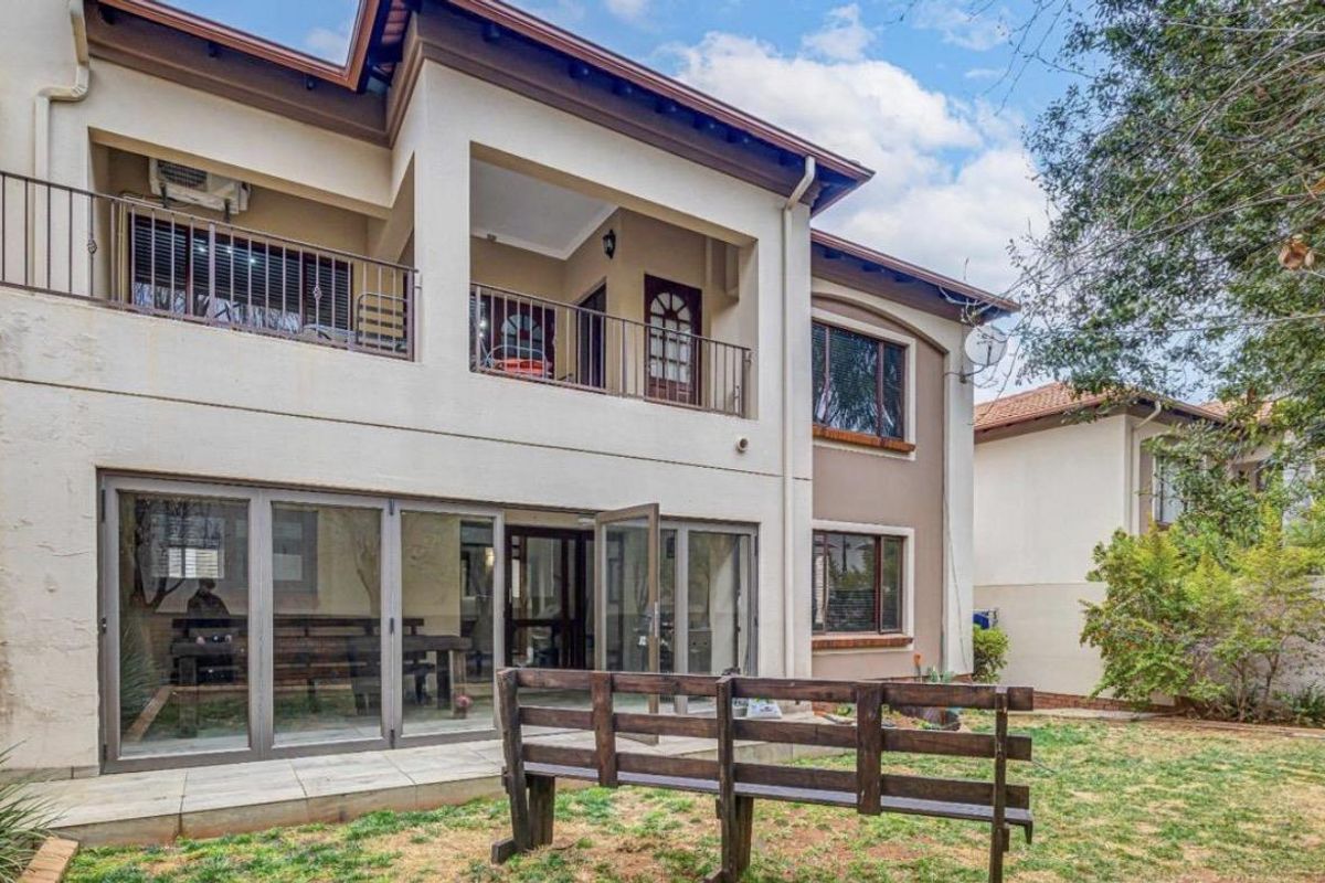 Rear view of a two-story townhouse featuring a ground-floor patio with glass sliding doors and an upper-level balcony with metal railings.