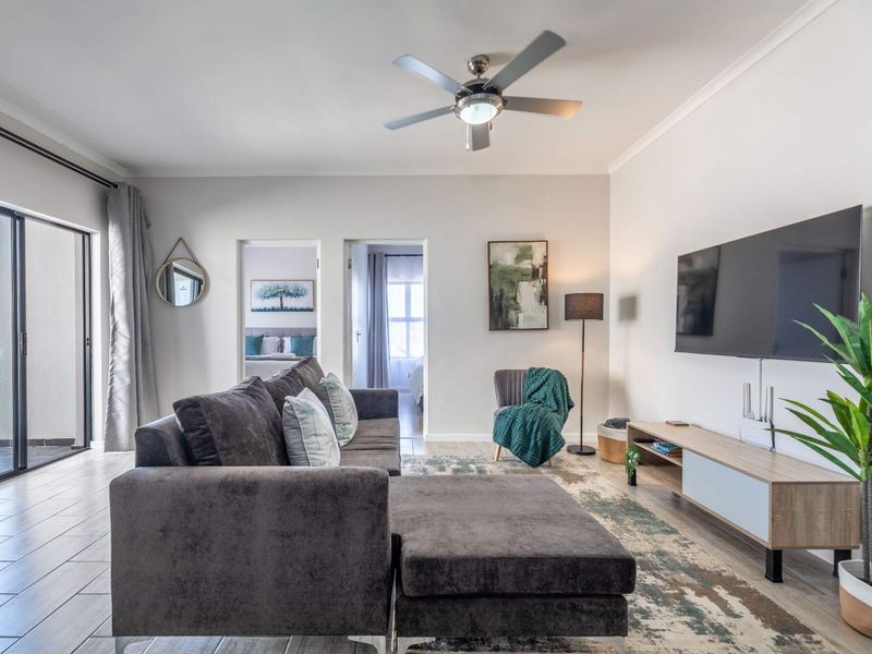 A bright and well-maintained living room featuring tiled flooring, a ceiling fan, and a large sliding glass door leading to an outdoor balcony.