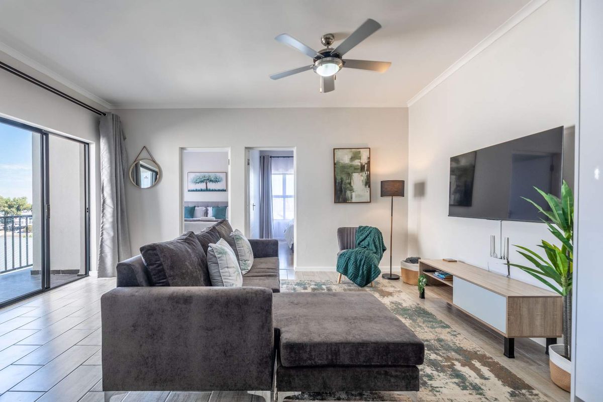 A bright and well-maintained living room featuring tiled flooring, a ceiling fan, and a large sliding glass door leading to an outdoor balcony.