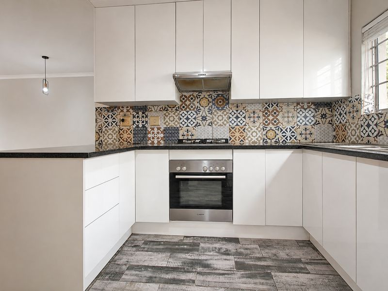 Modern kitchen featuring white cabinetry, granite countertops, a patterned tile backsplash, stainless steel oven, gas hob, and wood-look tile flooring.