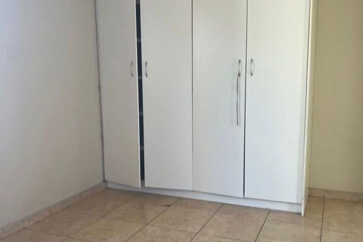 A simple bedroom featuring neutral tiled flooring and a large white built-in wardrobe with multiple doors.