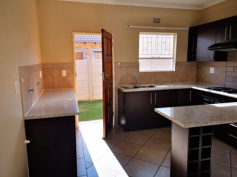 A functional kitchen featuring dark wood cabinetry, granite countertops, built-in hob with extractor, and direct access to the rear garden area.