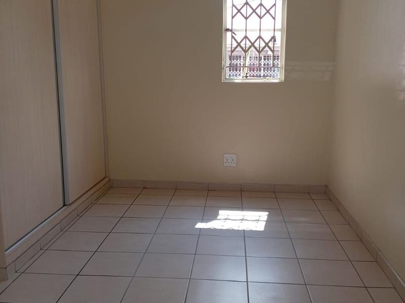 A clean, empty bedroom featuring neutral tiled flooring, a built-in wardrobe, and a window fitted with a security gate.