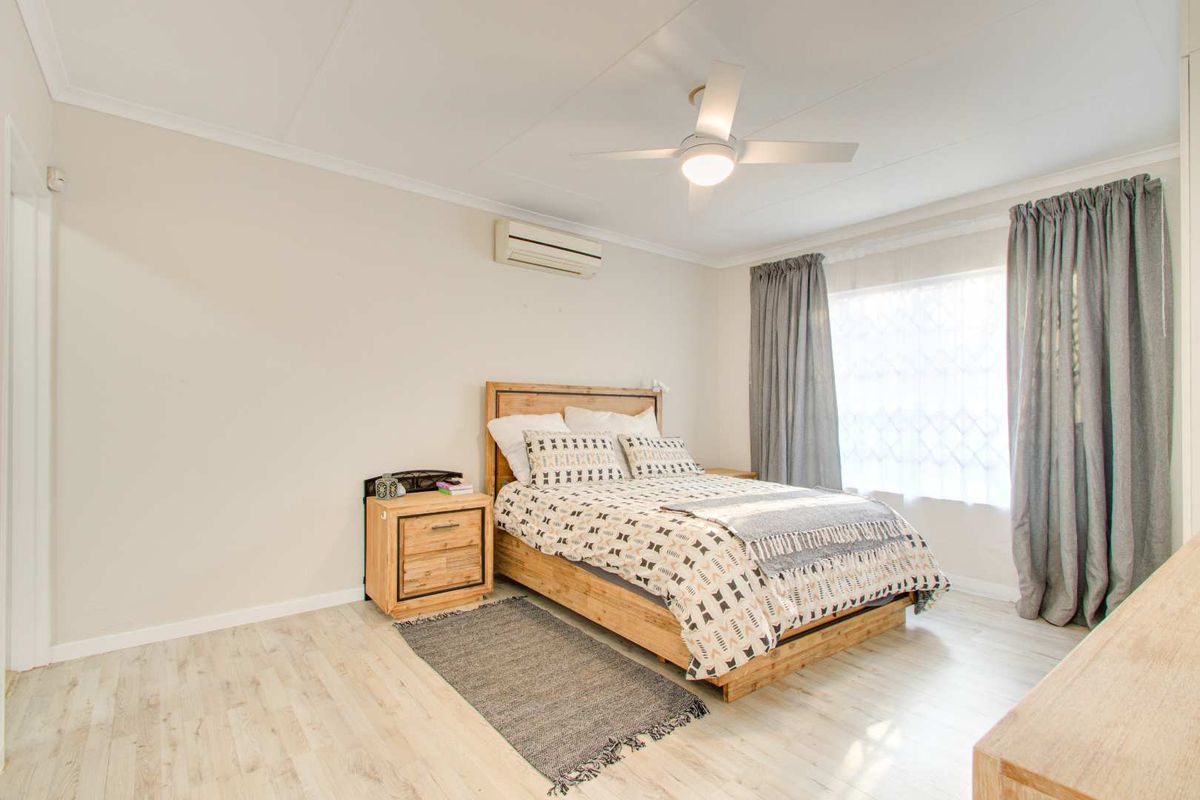 A well-maintained bedroom featuring light wood-look flooring, a ceiling fan, and a wall-mounted air conditioning unit.